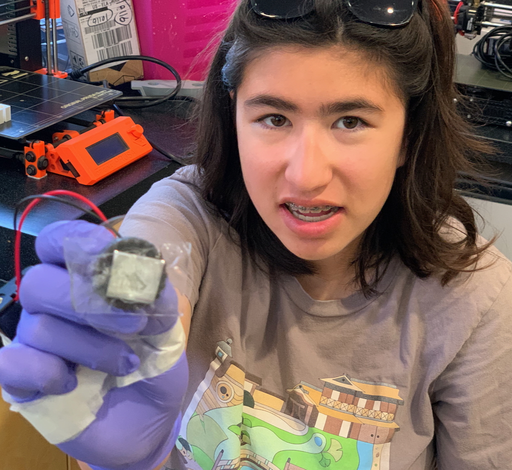 Chloe wearing purple disposable gloves holding a small gray item to camera