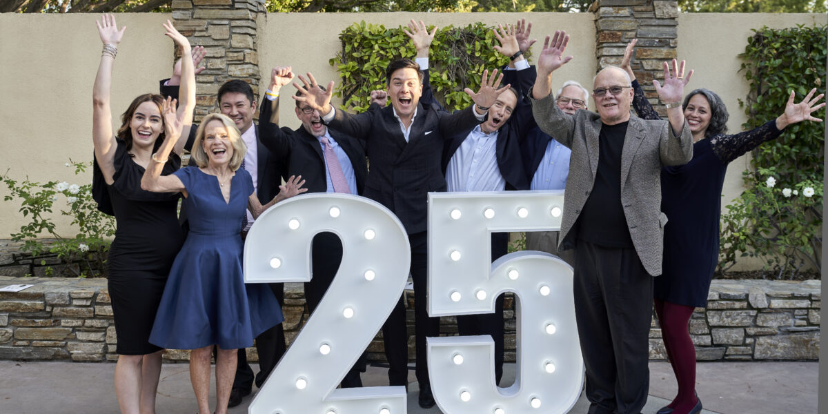 IEA Board members happily standing around marquee 25 lights with their hands raised in celebration